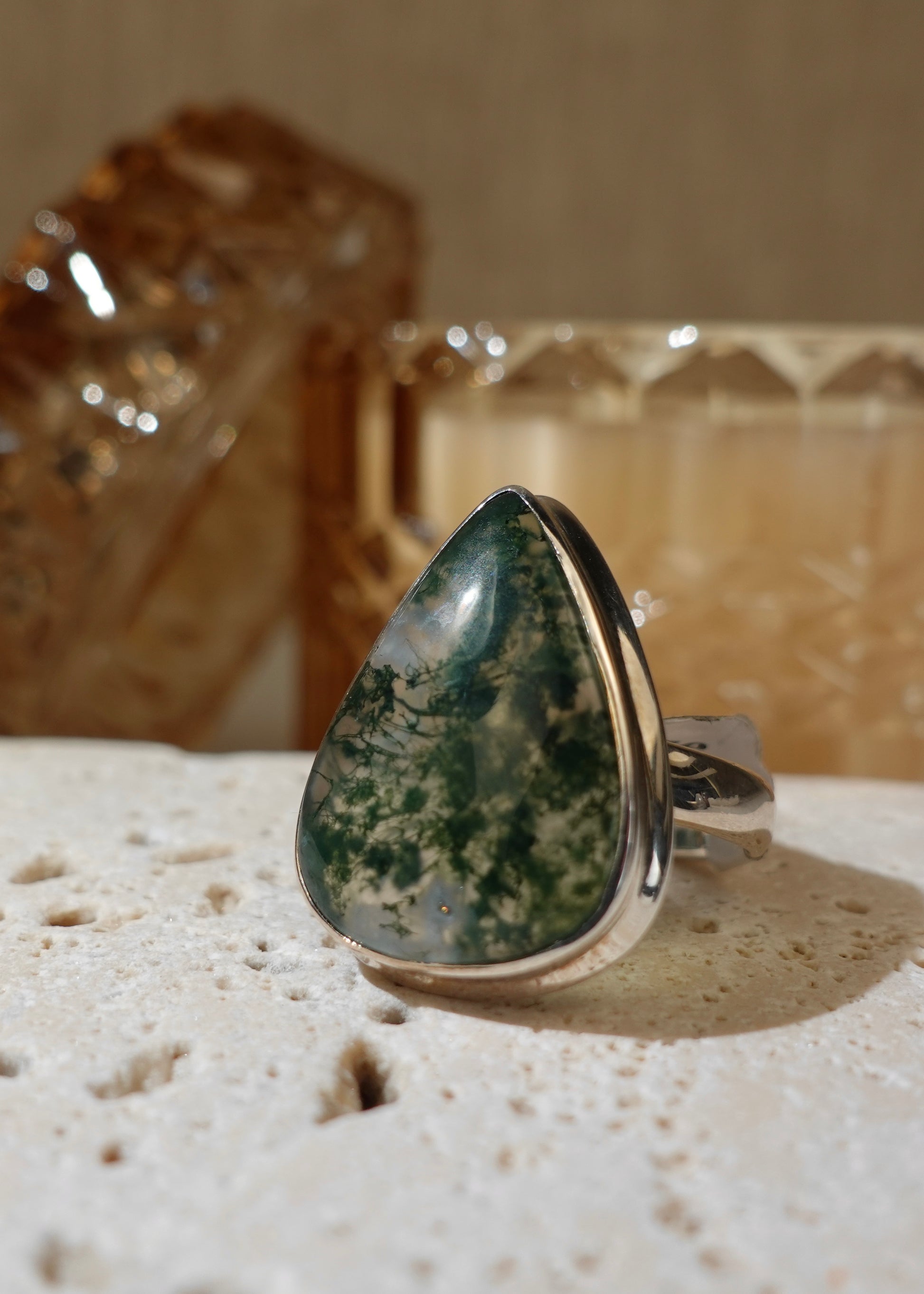 Moss Agate Ring on travertine display with glass background