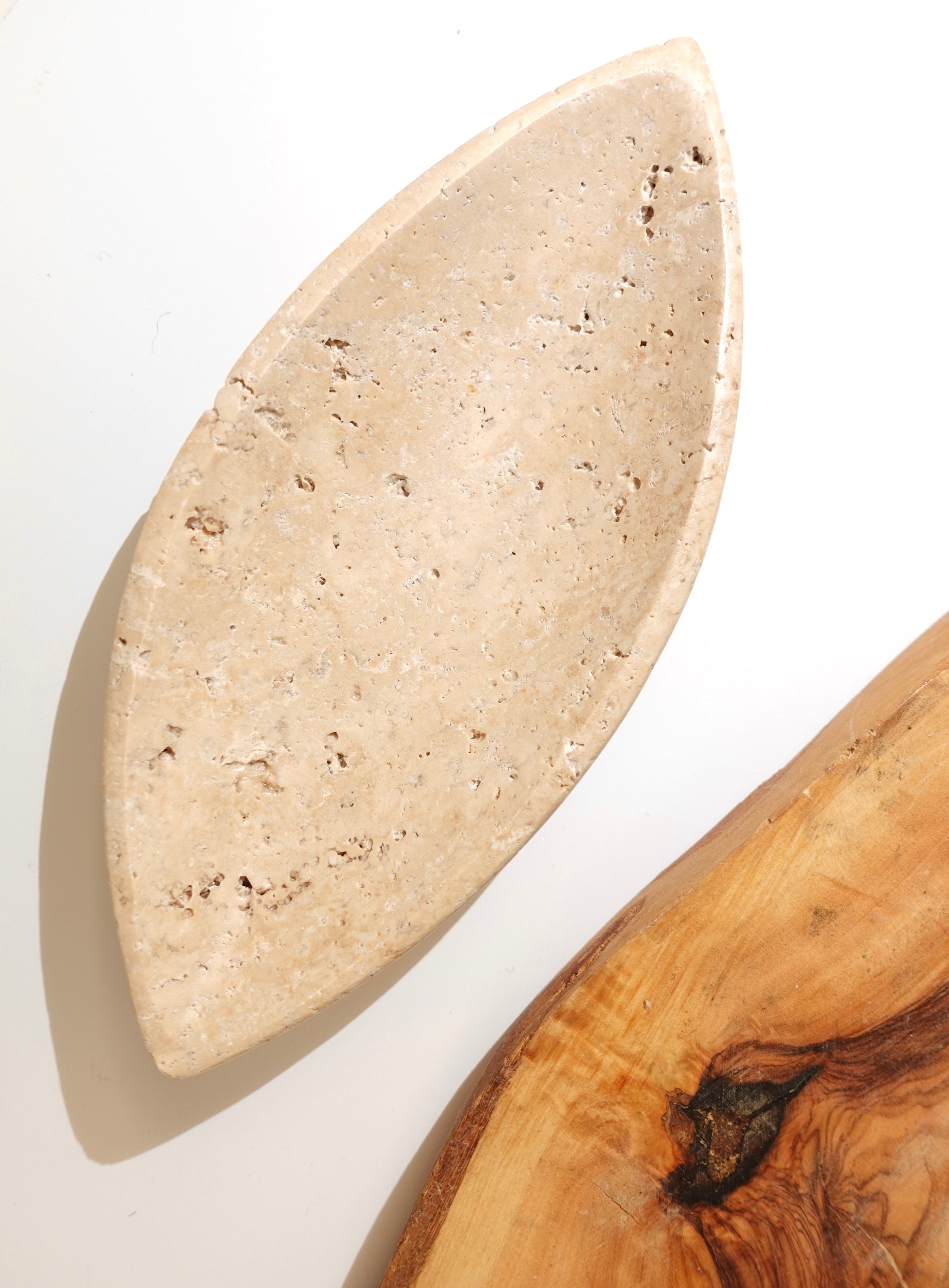 Travertine marguise shaped dish on white background next to wood slab for decor