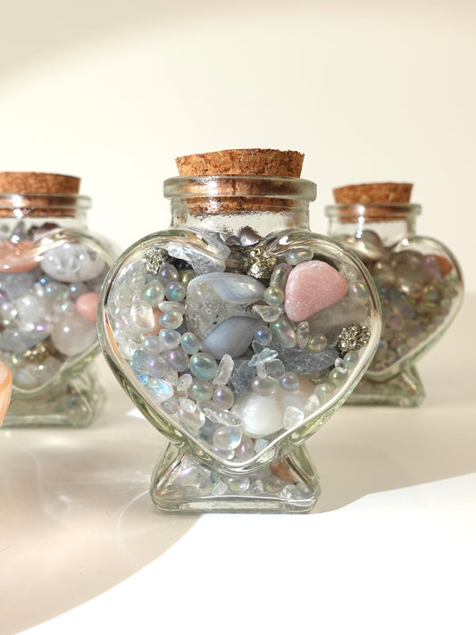 Heart-shaped glass jar filled with decorative stones on a white surface