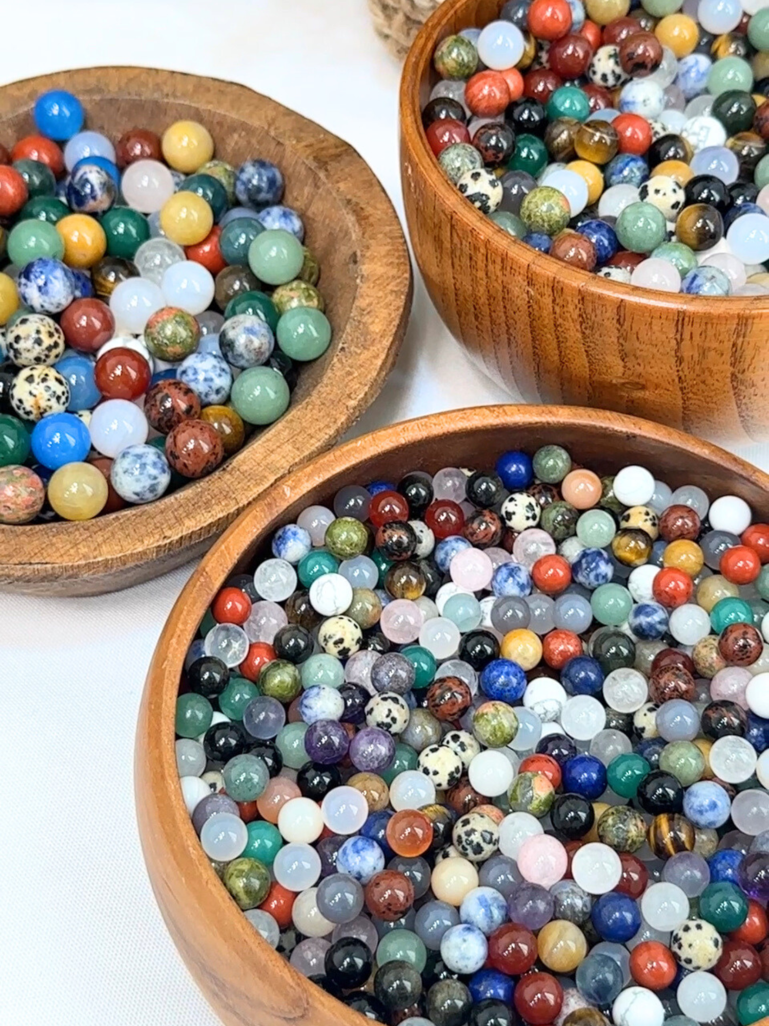 Three wooden bowls with mini spheres of diferent crystal materials.