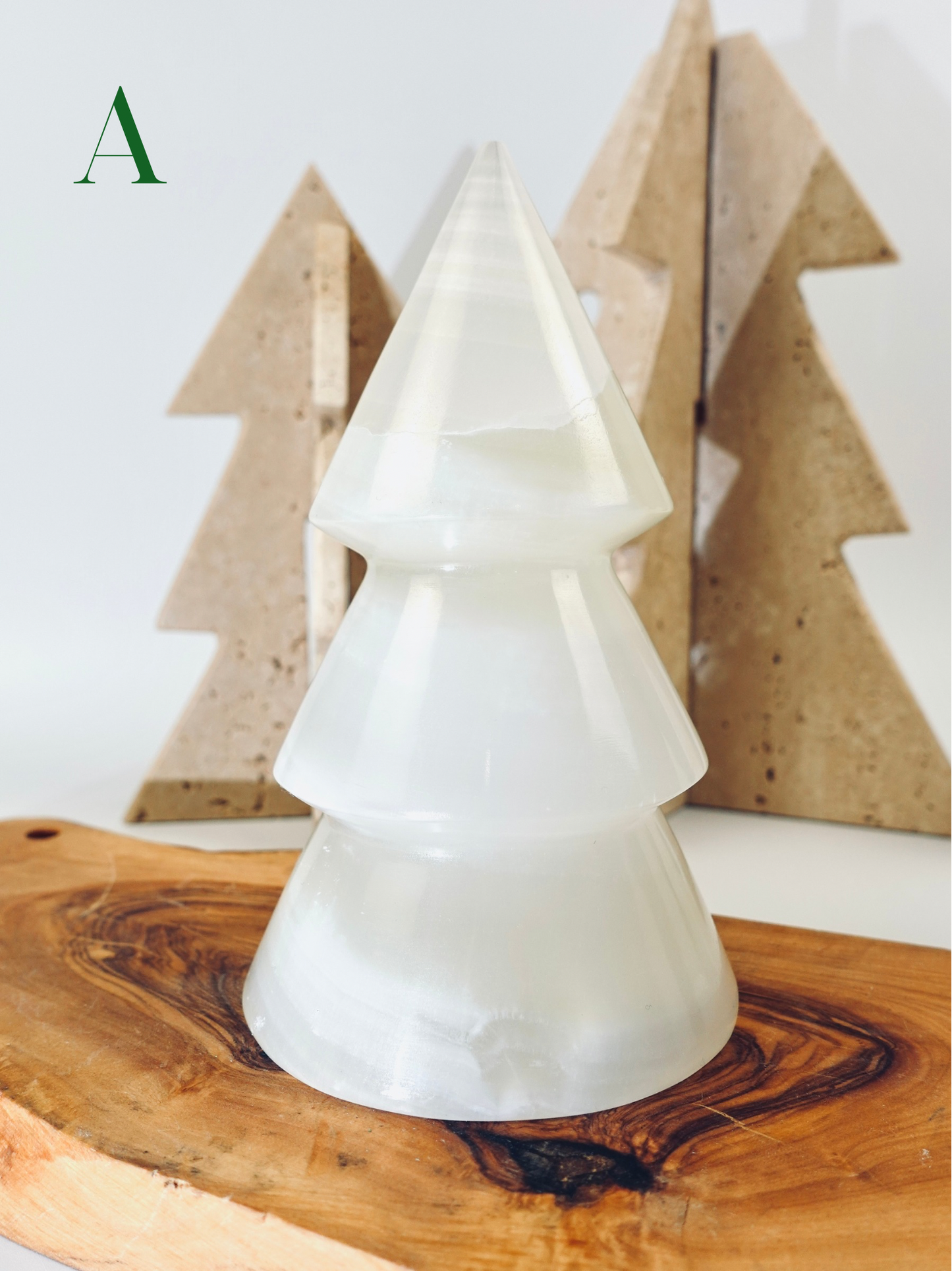 White ceramic Christmas tree on a wooden surface with wooden trees in the background