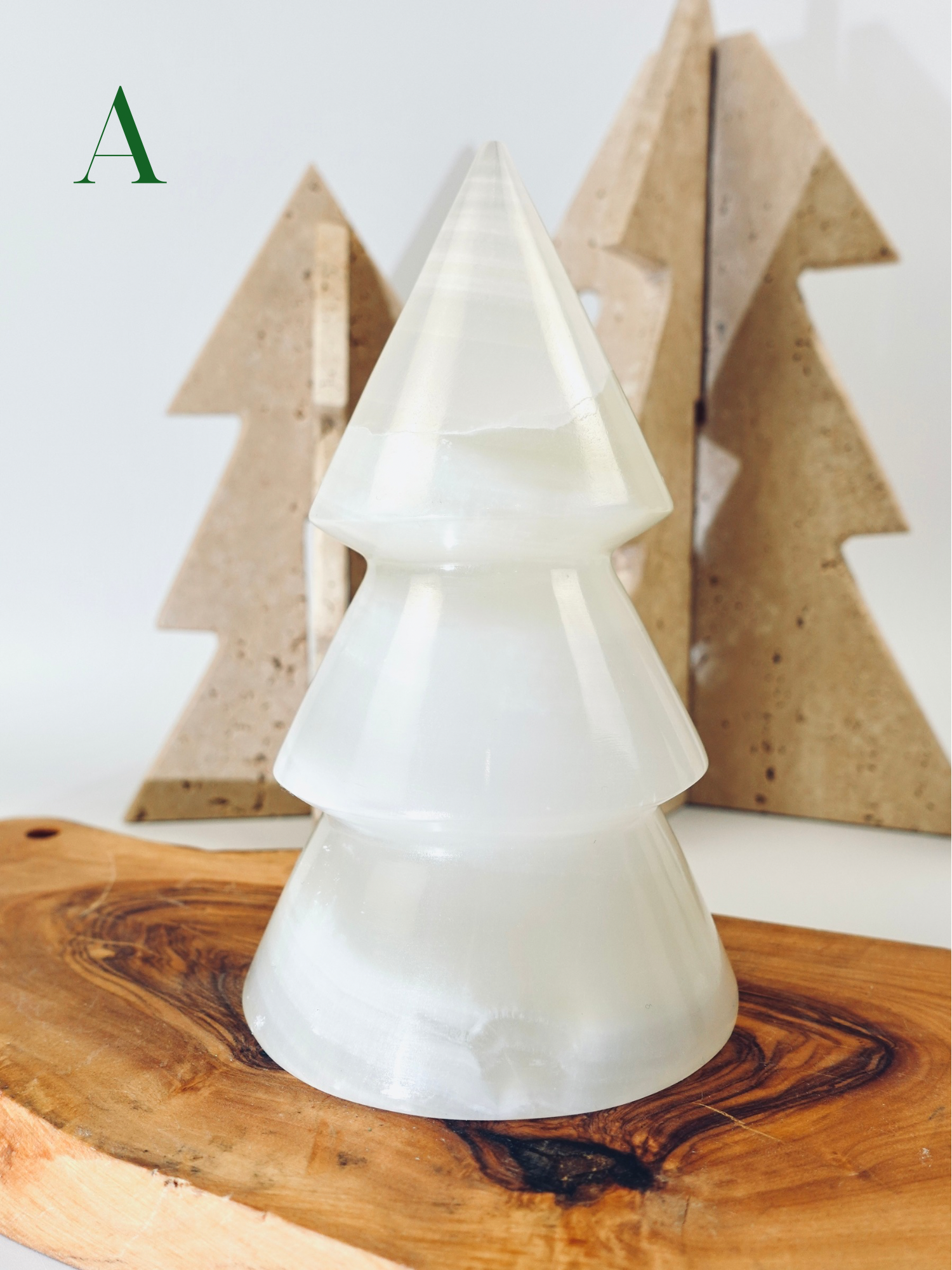White ceramic Christmas tree on a wooden surface with wooden trees in the background