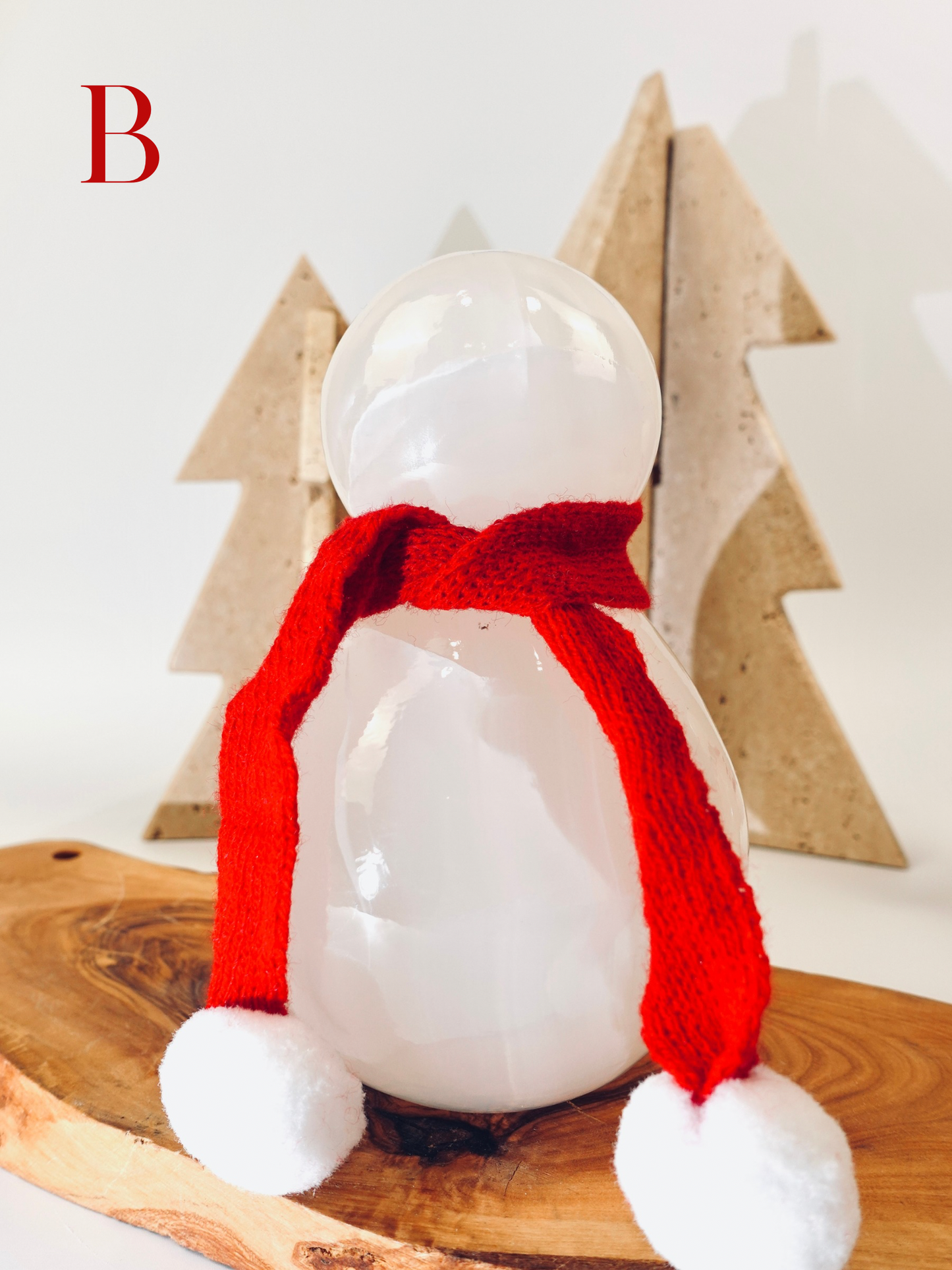 White ceramic penguin with a red scarf on a wooden surface with decorative trees in the background.