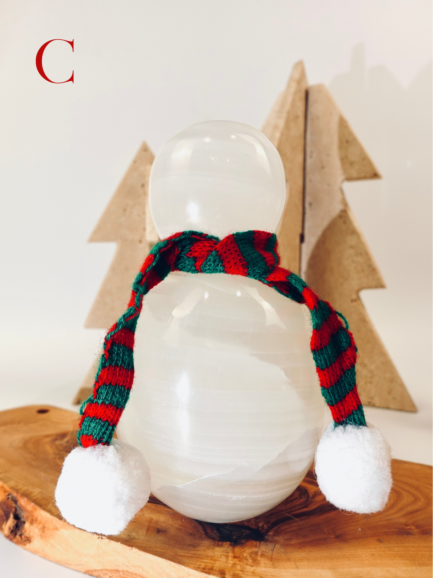 Snowman figurine with a red and green striped scarf and white pom-poms on a wooden surface.