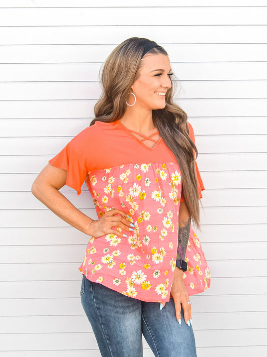 Side view, orange top with floral details and criss cross neckline. 