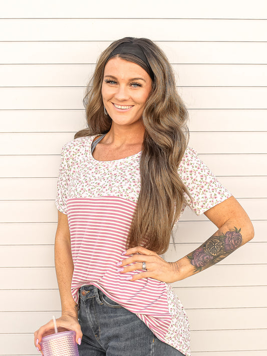 Front view of pink and white stripe top with floral top details tucked into jeans.