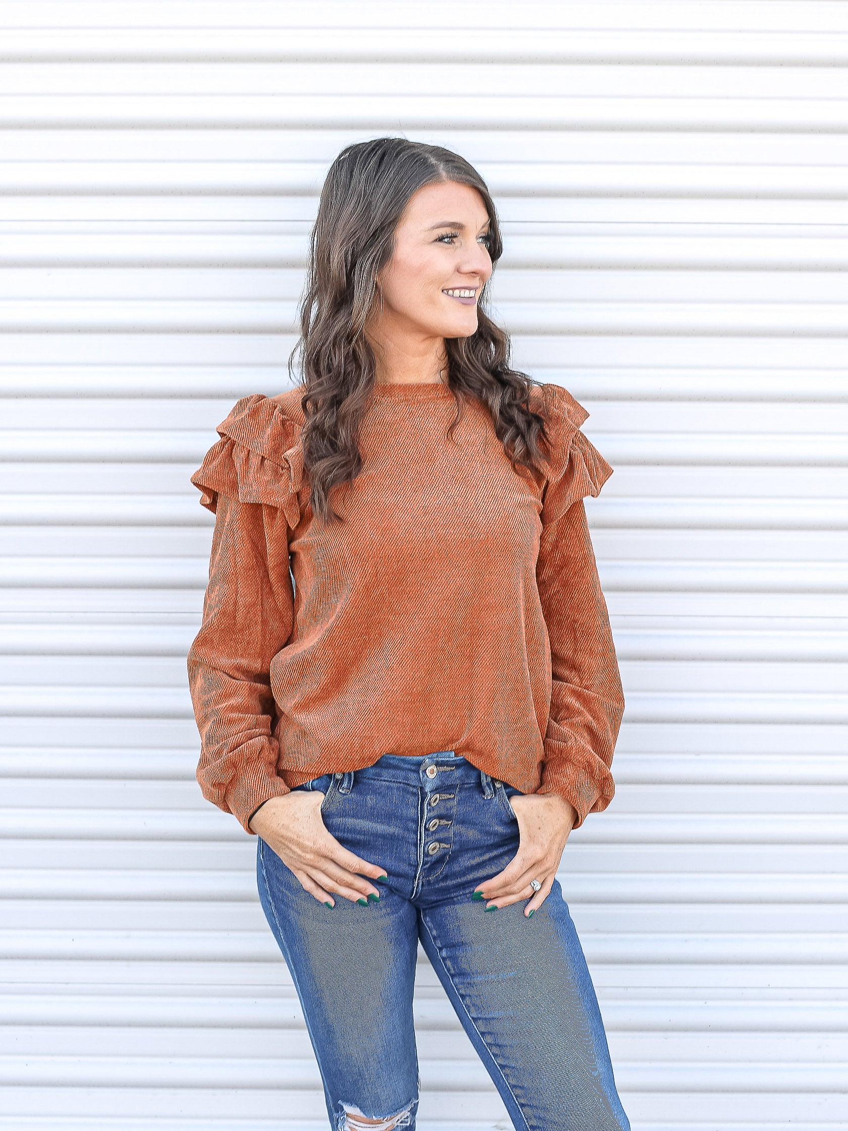 Rust colored ruffled shoulder sweater tucked into jeans