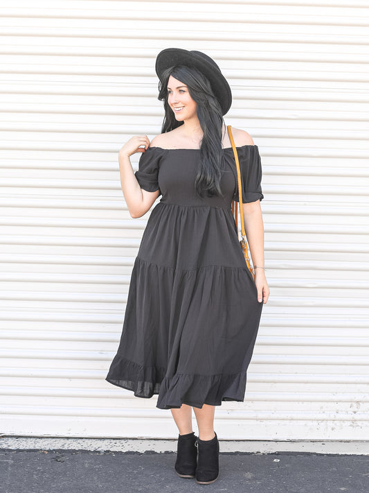 Off the shoulder black mini dress styled with boots and a hat