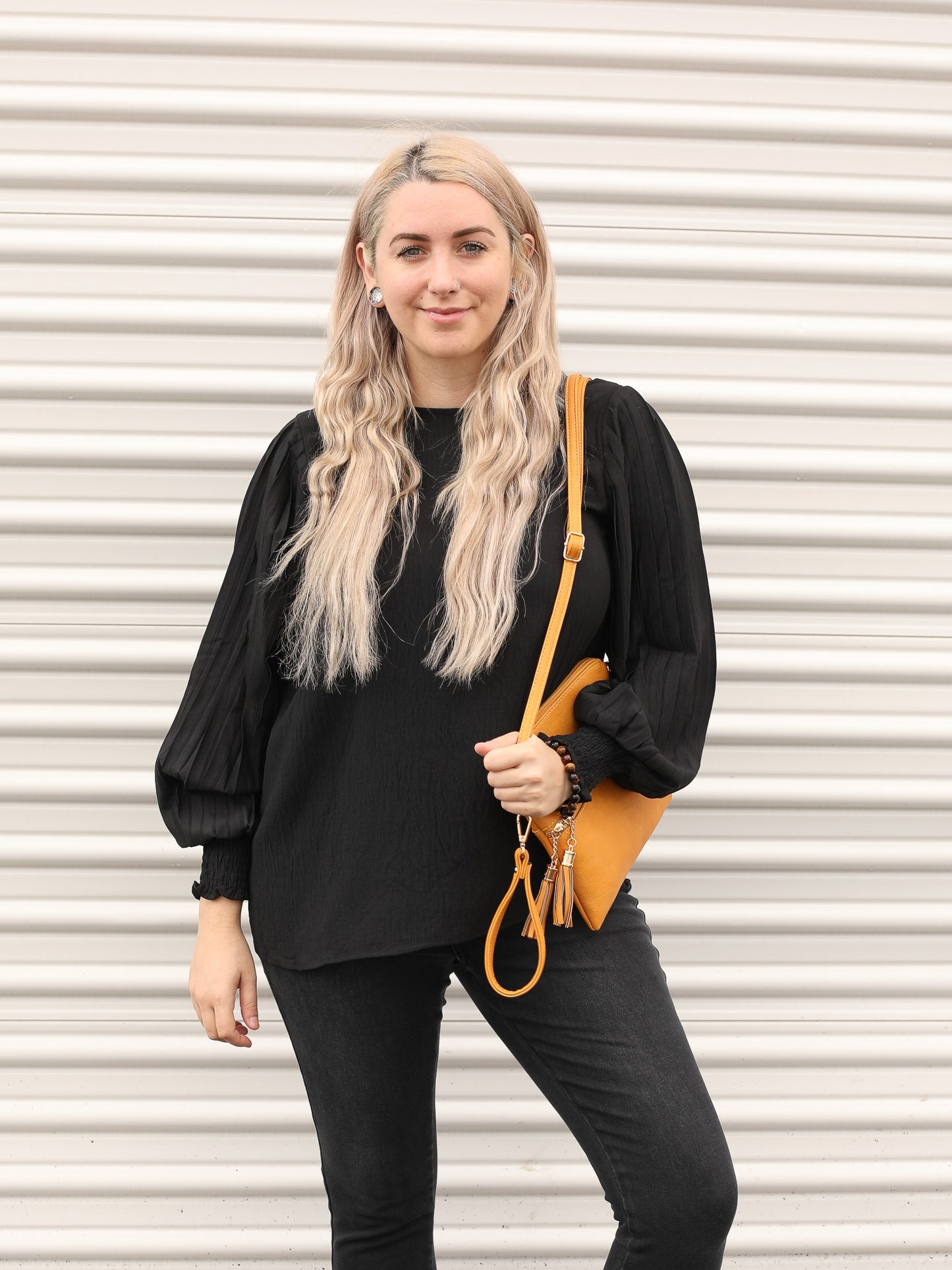 Black blouse with balloon textured sleeves and elastic around the wrist styled with black jeans and a mustard purse for a pop of color. 