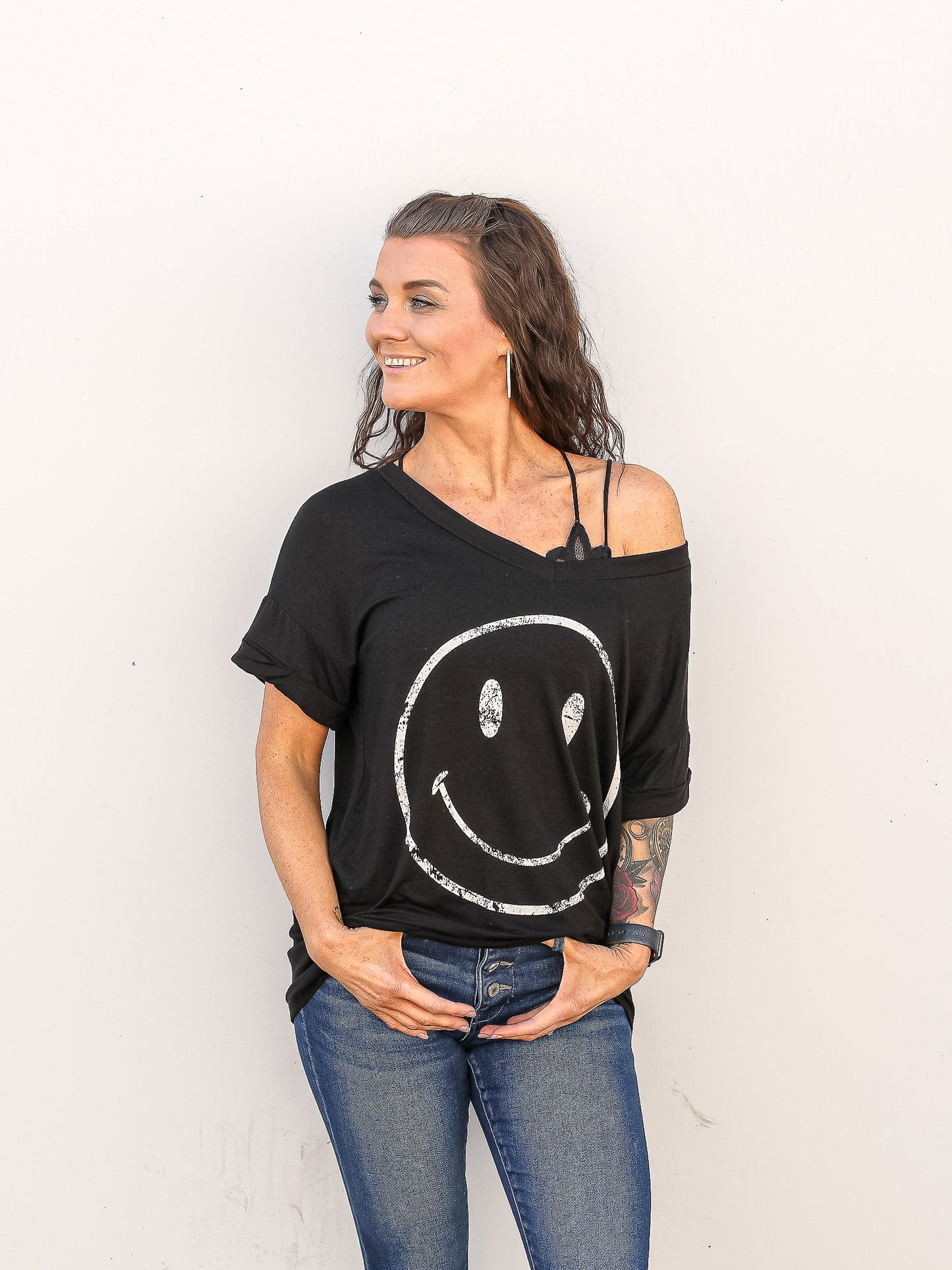 Black short sleeve smily tee pulled off the shoulder with denim pants. 